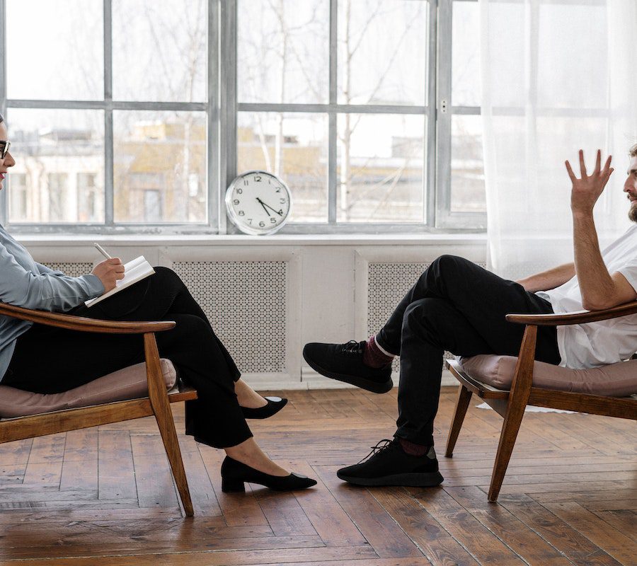 Person in Black Pants and Black Shoes Sitting on Brown Wooden Chair Person in Black Pants and Black Shoes Sitting on Brown Wooden Chair
